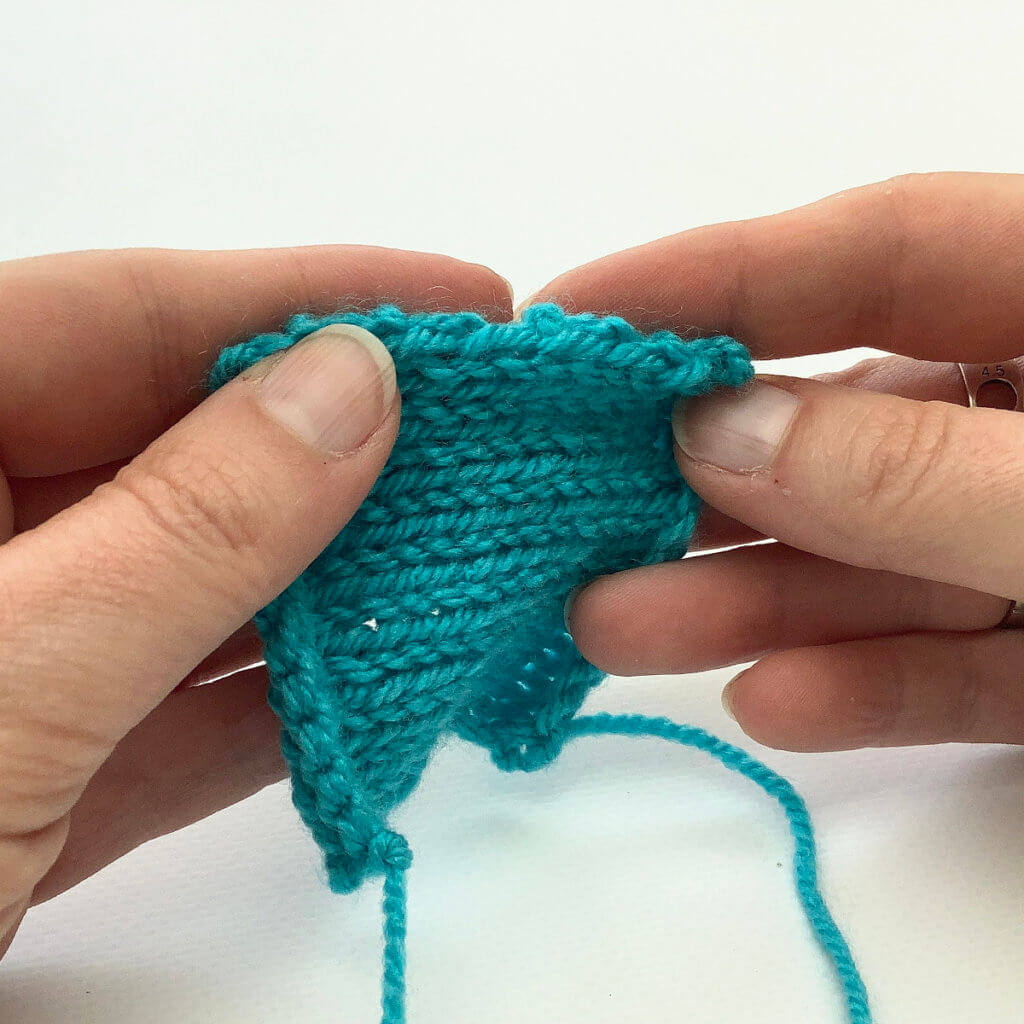 Turquoise knitted swatch held such that the edge is visible.