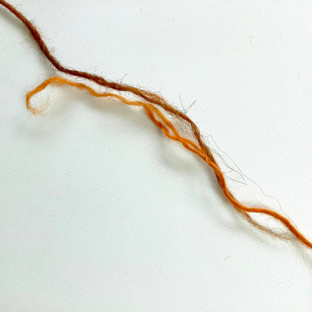 2 yarn ends (1 brown, 1 orange), placed together with an overlap.