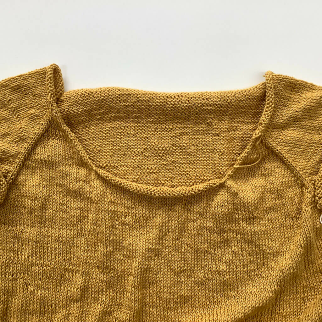 The yoke of an unfinished knitted tee in yellow yarn.