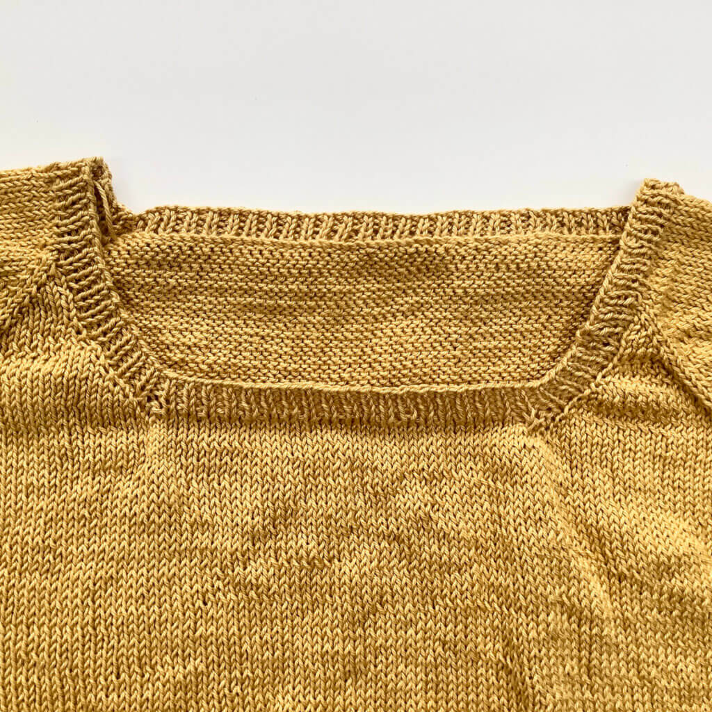 The yoke of a knitted tee in yellow yarn, with a finished neckband, shown as a flat lay.